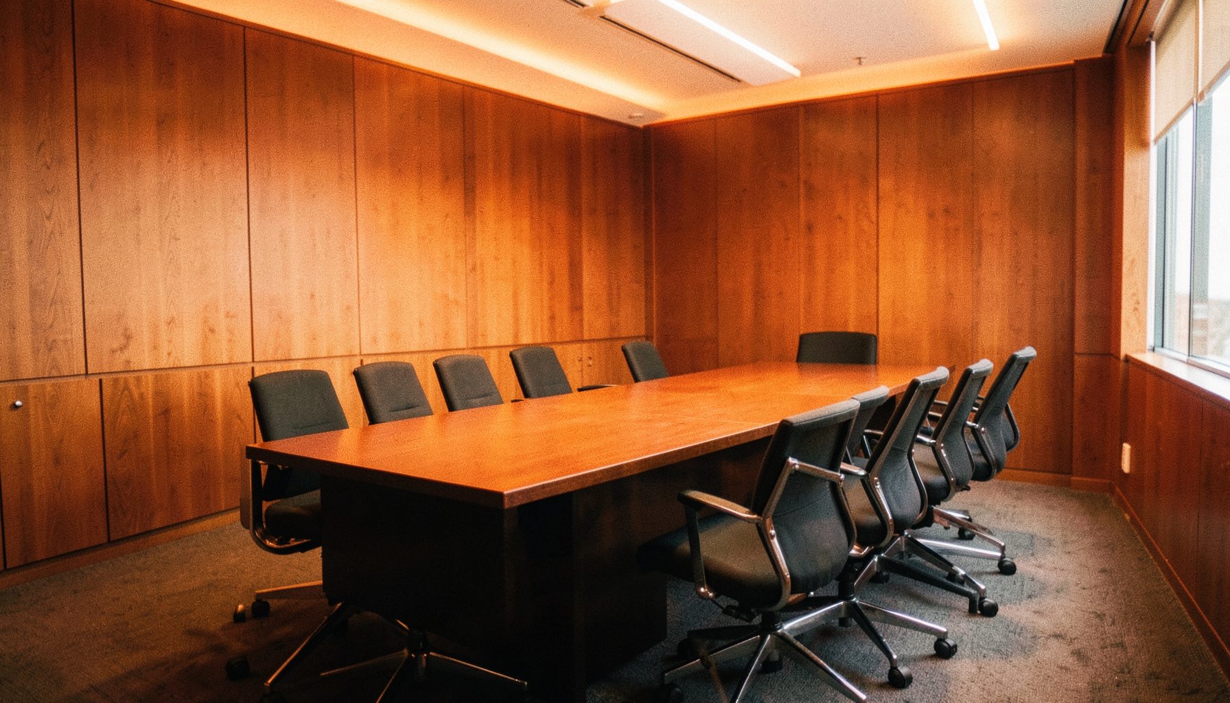 Warm interior of a professional conference room with wooden paneling and soft amber lighting, empty chairs arranged around a long table